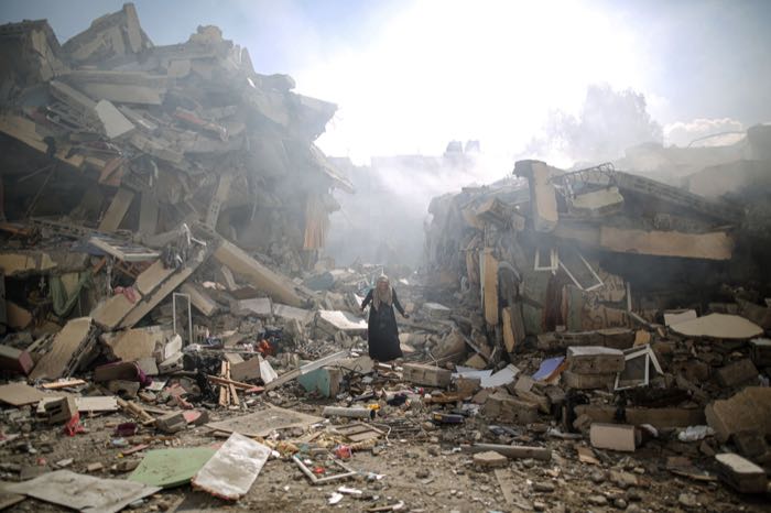 A woman walks through the rubble of a destroyed block.