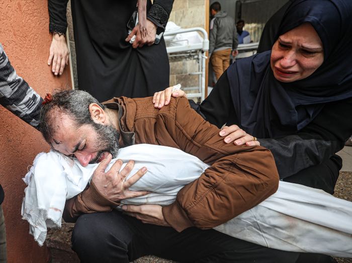 A father holds the shrouded body of his child outside the hospital.