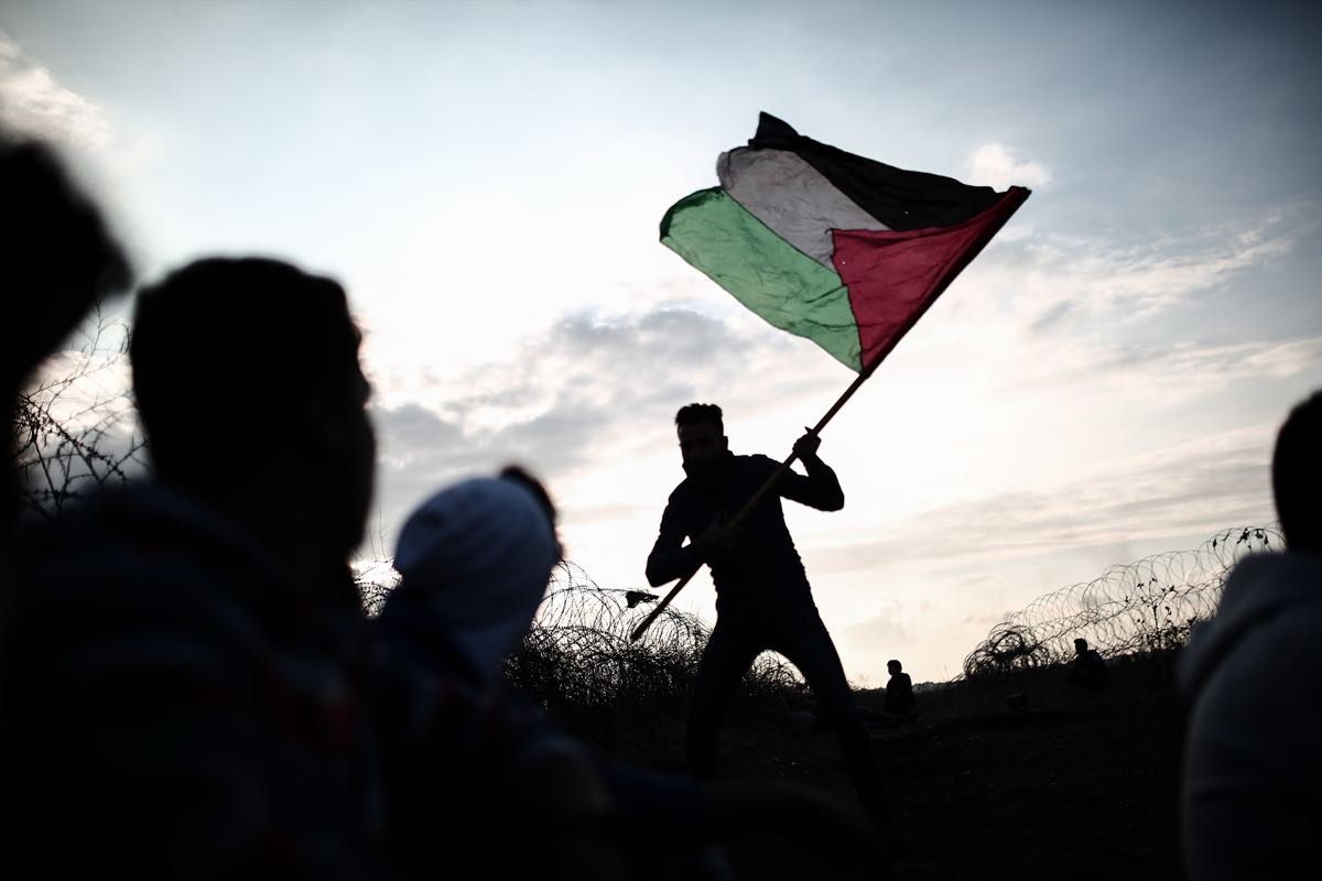 A man raises a flag at dusk, silhouetted against the last light.