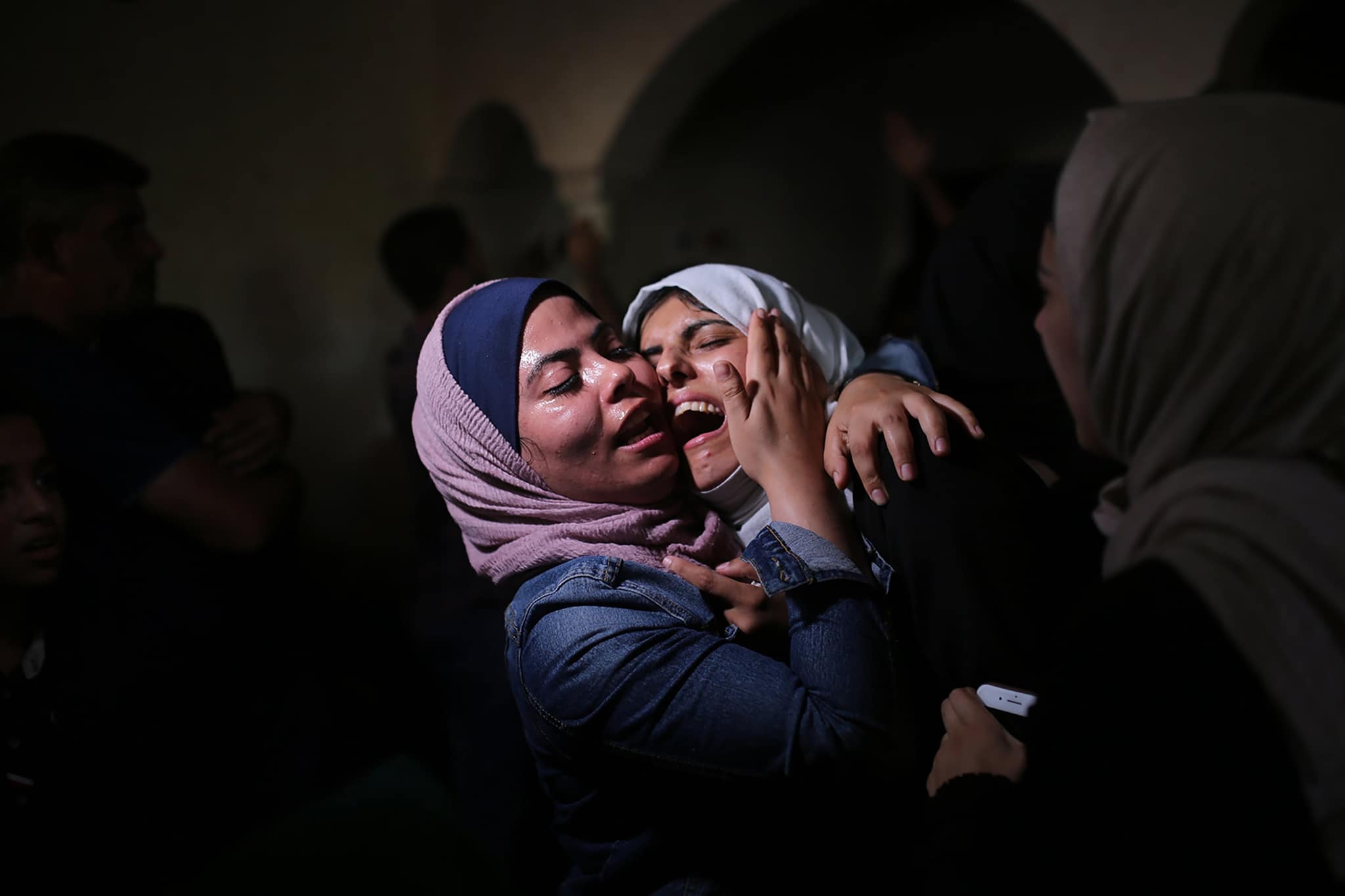 امرأتان تتعانقان، وقد غلبهما الانفعال، في ممر خافت الإضاءة.