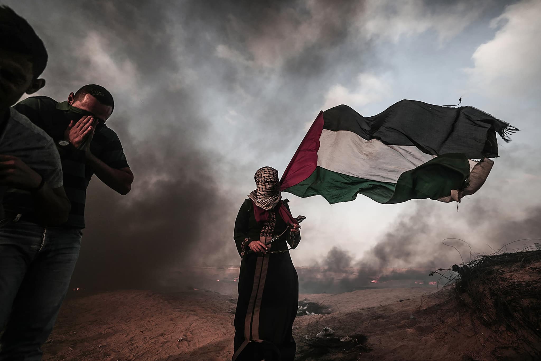 رجلان يحتميان من دخان أسود كثيف بينما يرفع أحدهما علمًا إلى جانبهما.